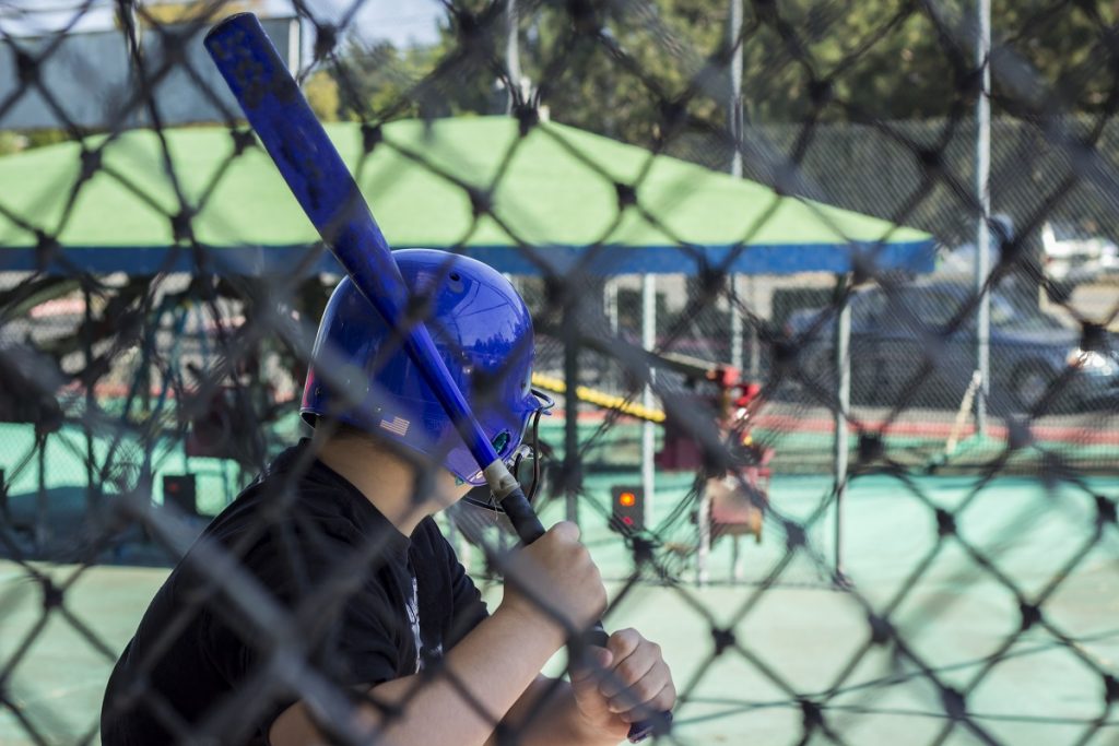 A teen boy at a batting cage getting ready to hit.