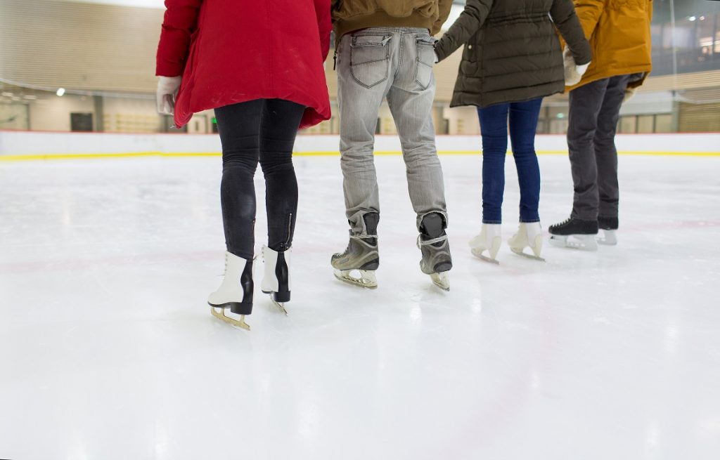 people, friendship, sport and leisure concept - close up of happy friends skating on ice rink